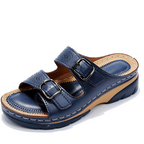 Dark blue slide sandal with metal buckles and tan detailing around the footbed.