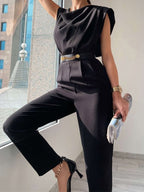 Black draped-neck jumpsuit showing the trouser legs while seated.
