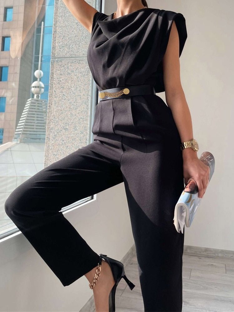 Black draped-neck jumpsuit showing the trouser legs while seated.