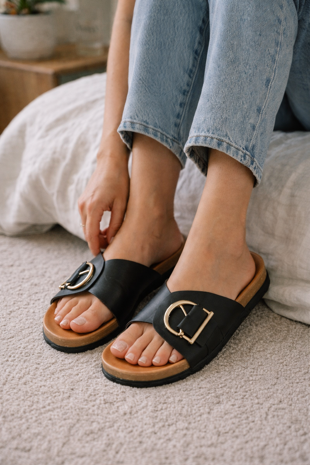 Close view of black slip-on sandals with broad straps and gold-coloured metal details.