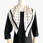 Cream scarf with black spots and a dark border draped on a mannequin.
