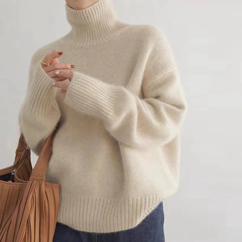 Cream-toned sweater with a high ribbed neckline and long sleeves, worn with jeans.