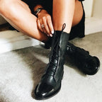 Person tying the laces of a black boot with a glossy toe cap.