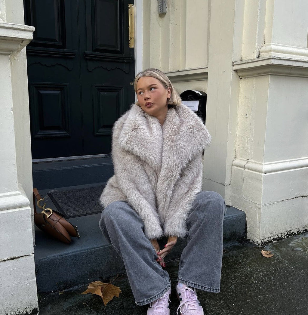 Pale faux-fur jacket worn while seated on steps.