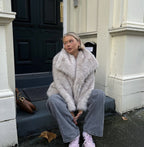 Pale faux-fur jacket worn while seated on steps.