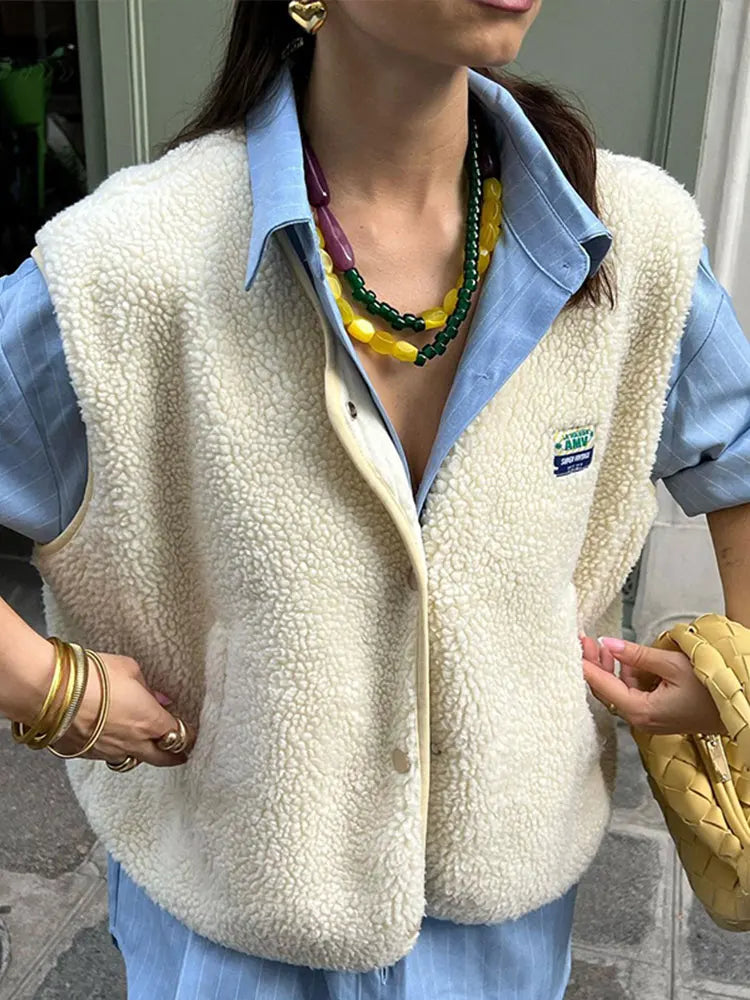 Cream curled-pile gilet worn over a blue shirt, with a small chest patch.
