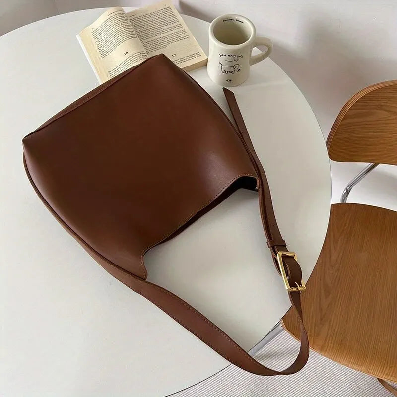 Brown shoulder bag laid flat with its wide strap extended.