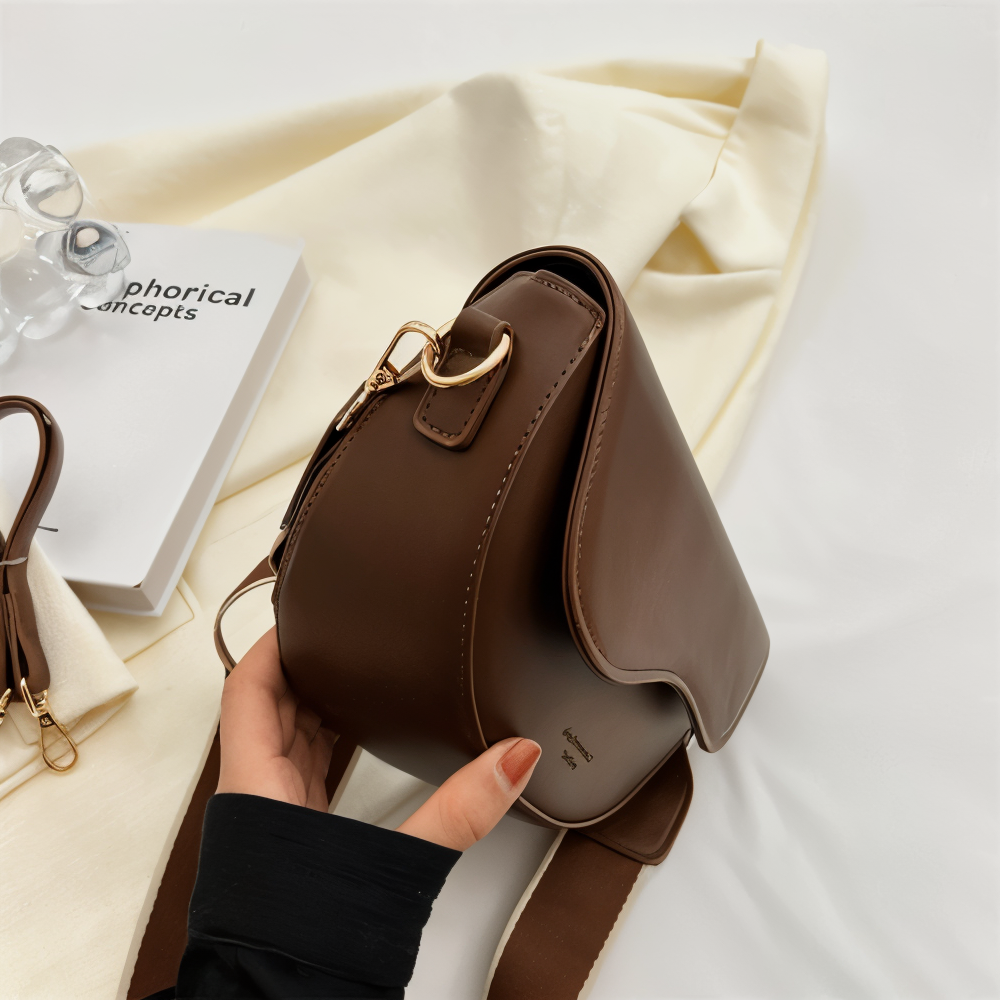 Side view of a brown bag showing the strap attachment and curved flap.