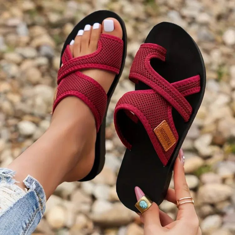 Red mesh-strap sandals with toe posts, one worn and one held.
