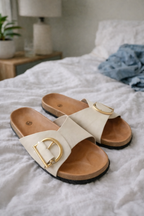 Beige slides displayed with broad crossed-look straps and metal details.