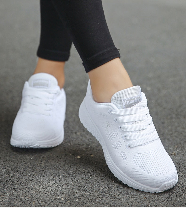 White lace-up trainers worn on a grey surface.