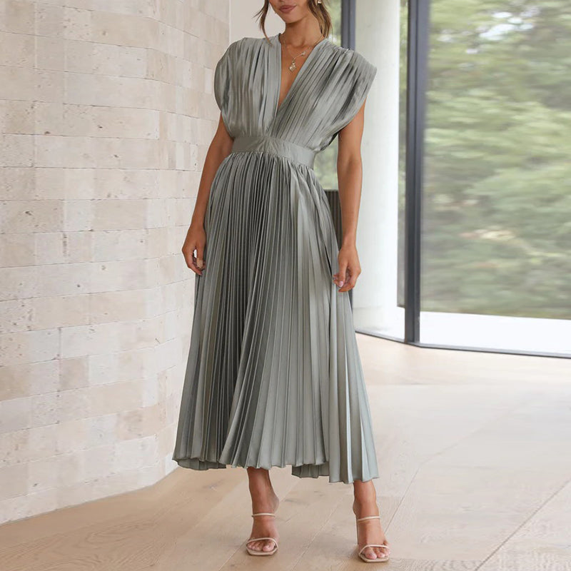 Grey pleated midi dress shown standing beside a window.