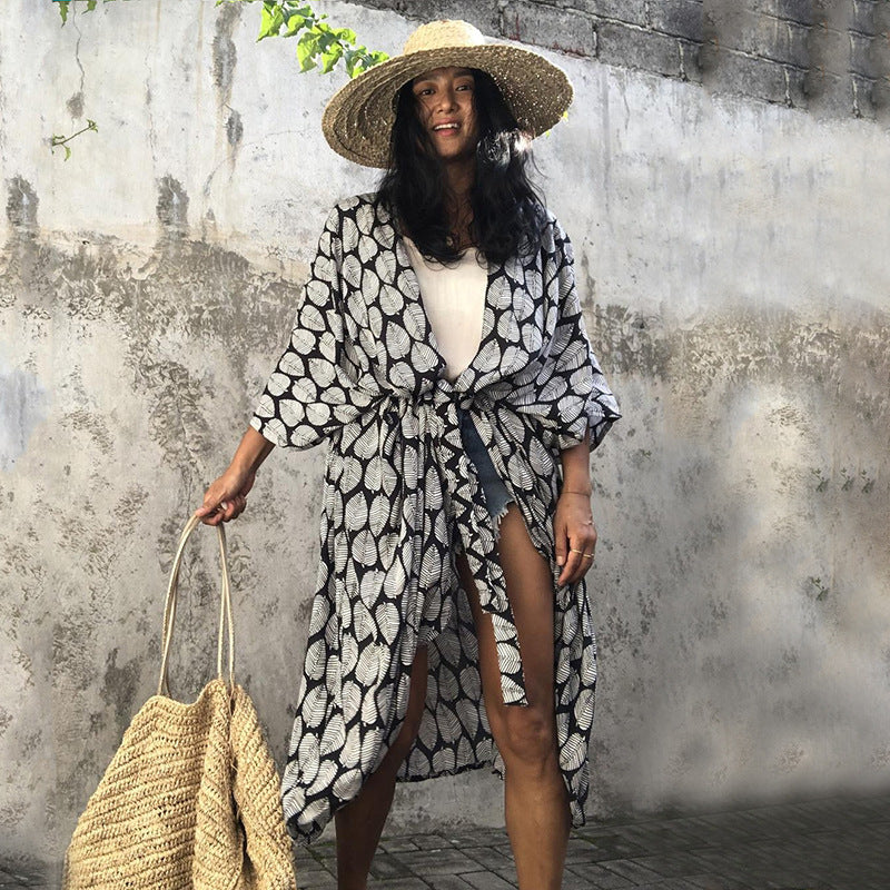 Black leaf-print cover-up loosely tied over a white swimsuit.