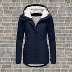 Navy coat with a cream hood lining and two angled pockets against a brick wall.