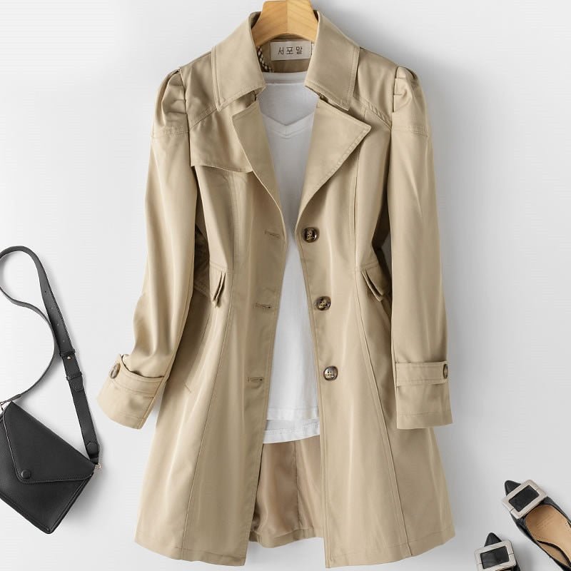 Khaki jacket with a three-button front, long sleeves and side pockets, hanging against a light wall.