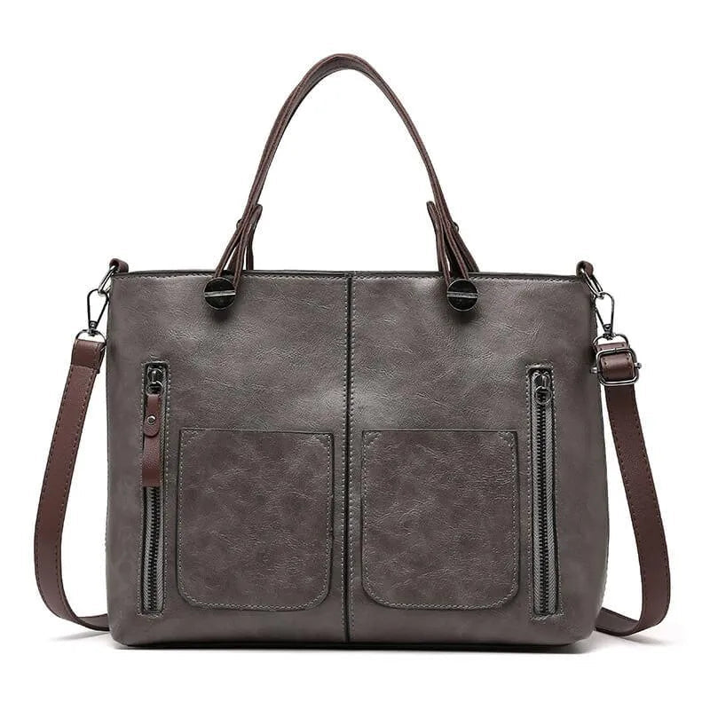 Grey handbag with front pockets and brown handles and strap.