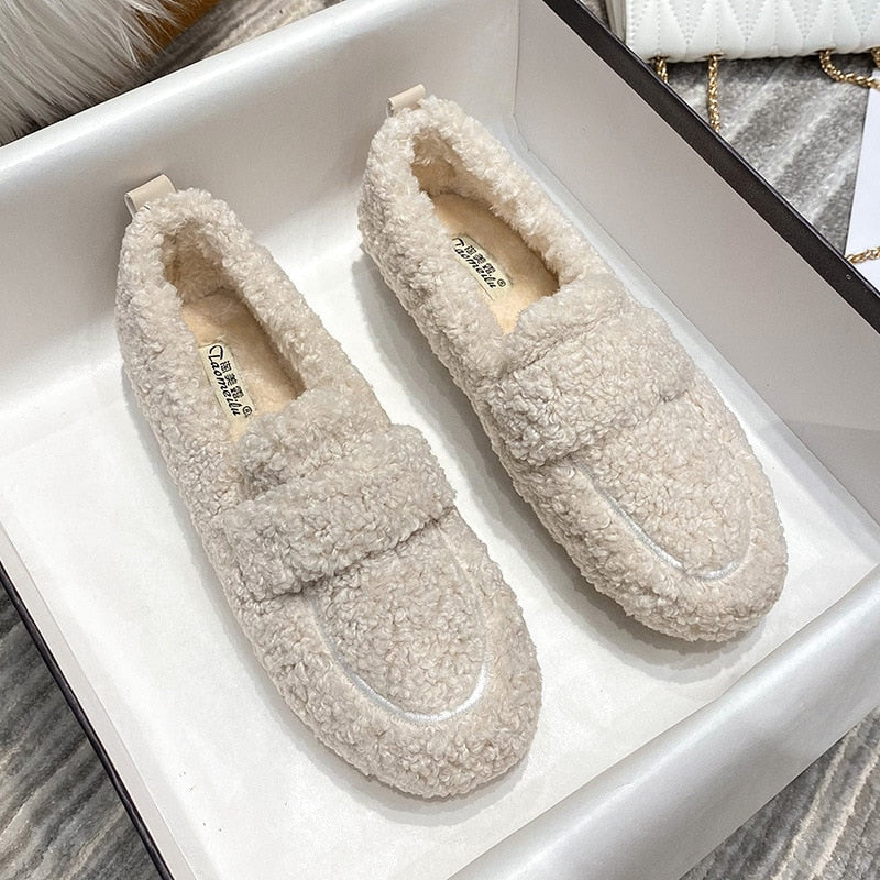 Cream plush slippers displayed in a box with source lettering visible on the insoles.