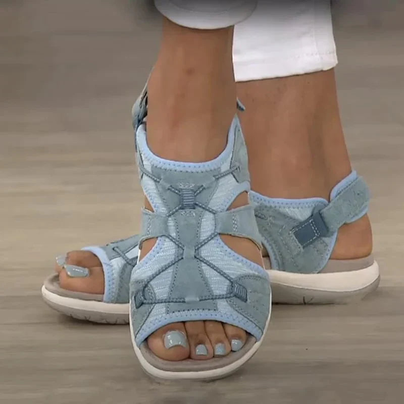 Light blue open-toe sandals with cut-out sides worn with white trousers.