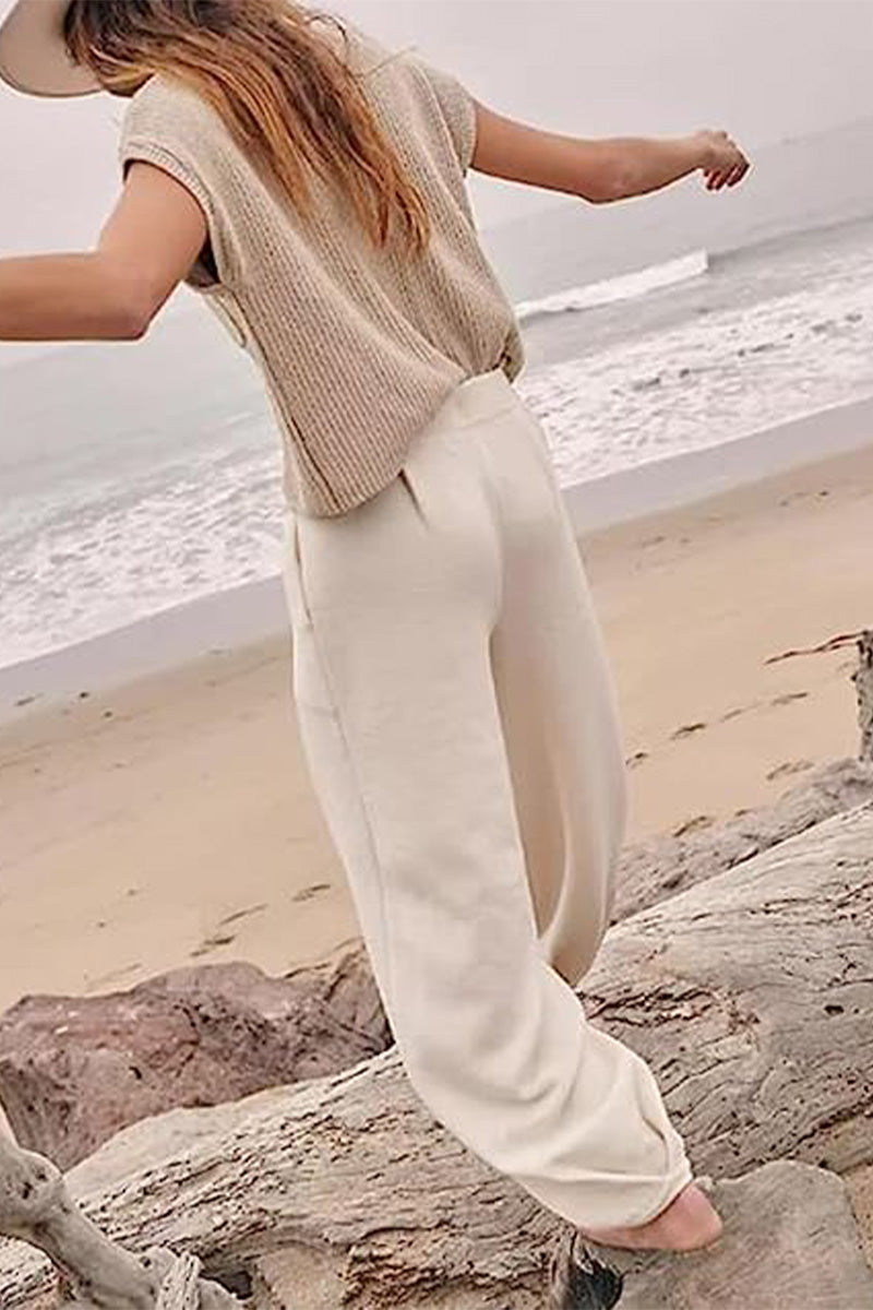 Rear view of a beige knit top and cream roomy trousers at a beach.
