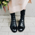 Black boots worn with a pale skirt, showing lace-up fronts and shiny toe caps.
