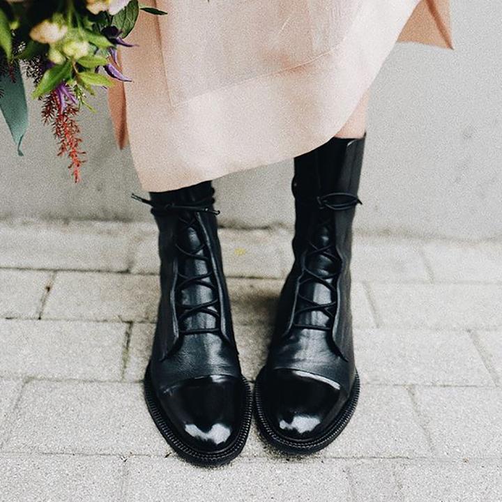 Black boots worn with a pale skirt, showing lace-up fronts and shiny toe caps.