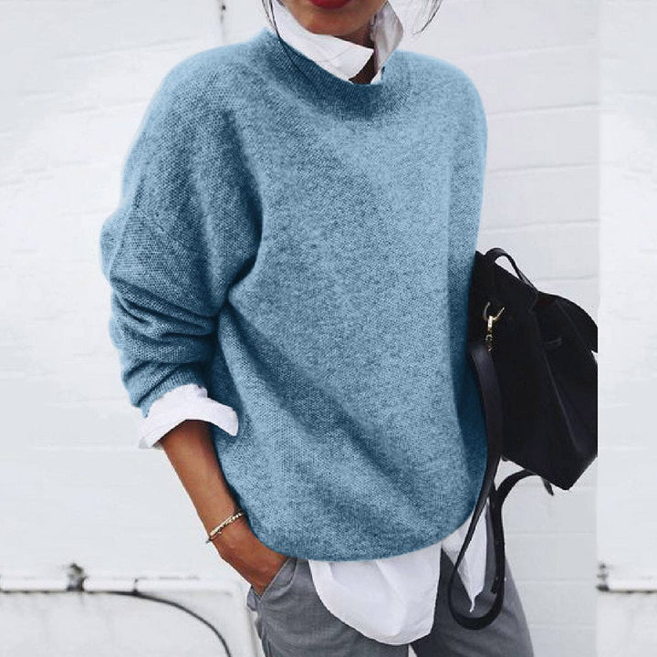 Blue jumper with dropped shoulders and long sleeves worn with grey trousers.
