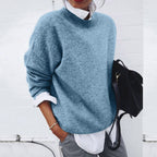 Blue jumper with dropped shoulders and long sleeves worn with grey trousers.
