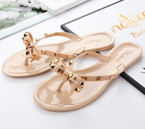Pale pink glossy sandals with studded straps and bows.