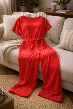 Red jumpsuit laid on a sofa, showing short sleeves, a gathered waist and long legs.