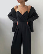 Black jumpsuit worn with a jacket resting on the shoulders.