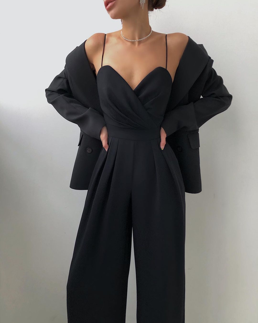 Black jumpsuit worn with a jacket resting on the shoulders.