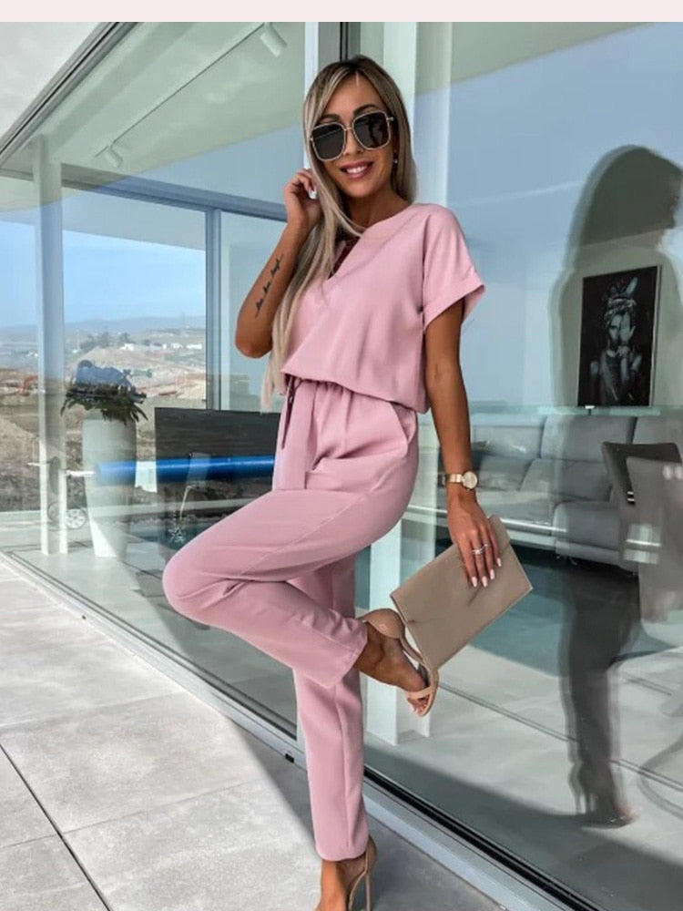 Pink short-sleeve jumpsuit shown while seated.