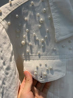 Close view of beads on the shoulder and pocket of a white denim jacket.