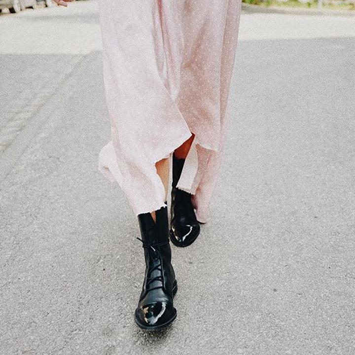 Overhead view of black lace-up boots beneath a flowing pale dress.