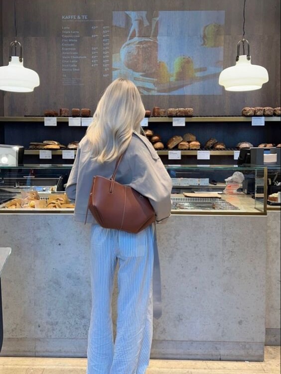 Woman at a cafe counter carrying a brown tote over one shoulder.