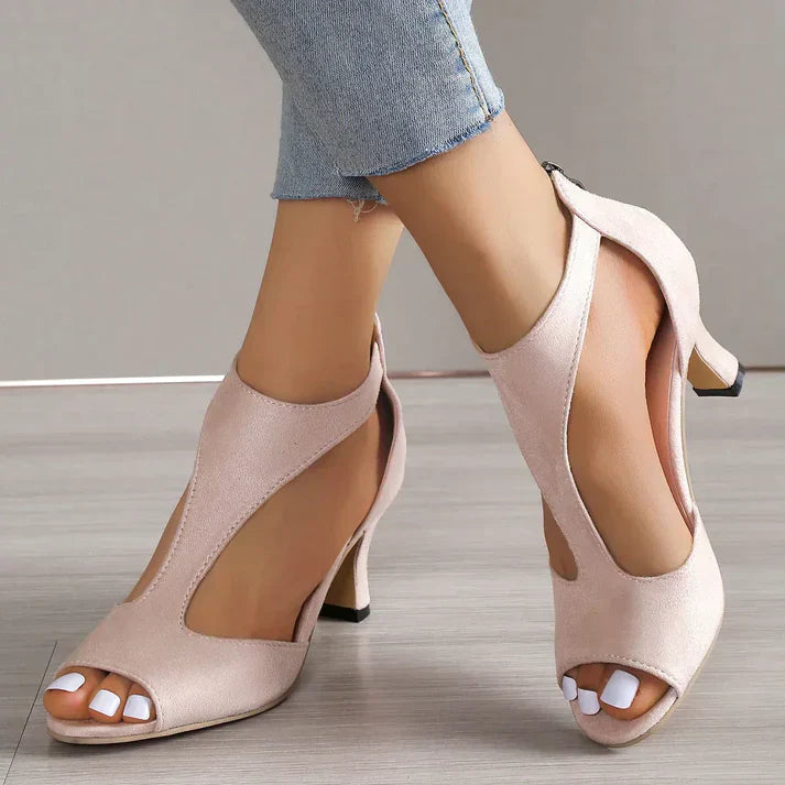 Pink peep-toe heels with curved side cutouts and shaped heels, worn with cropped jeans.