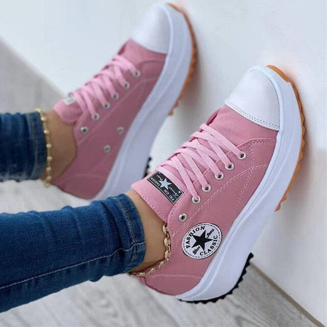 Pink trainers with white laces and a round star patch.