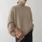 Taupe roll-neck sweater with long sleeves and ribbed trim, shown with a woven clutch.
