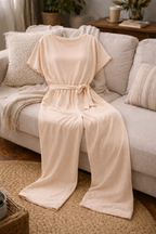 Beige wide-leg jumpsuit with short sleeves and a matching belt, arranged on a sofa.