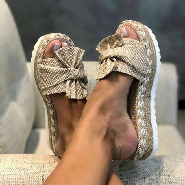 Beige bow slide sandals with woven-texture straps and rope-like platform edges.