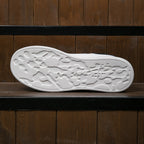 Underside of a white trainer with irregular recessed tread shapes.