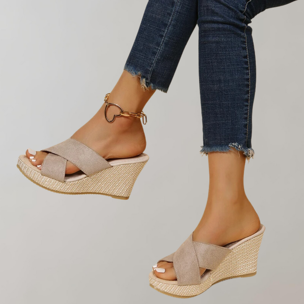 Pale beige wedge sandals with crossed straps and open backs.
