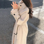 Close-up of beige coat with a point collar and buttoned cuff tab.