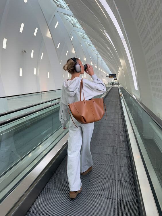 Woman wearing headphones with a brown tote over her shoulder on a moving walkway.