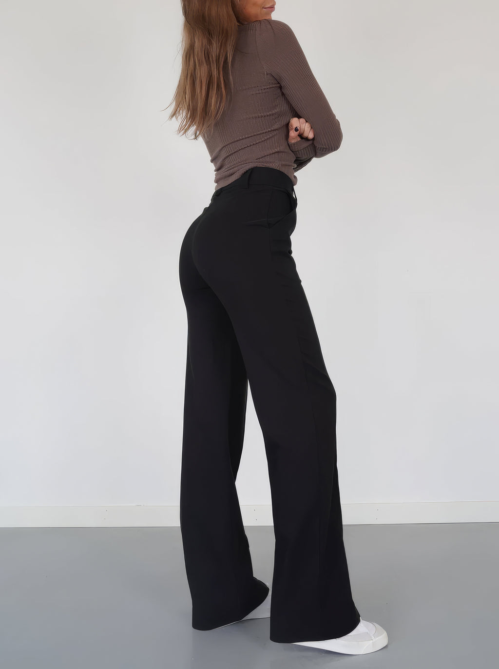 Side view of black full-length wide-leg trousers worn with white trainers.