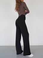 Side view of black full-length wide-leg trousers worn with white trainers.