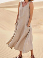 Beige-toned sleeveless dress with a rounded neckline and large front pockets, shown outdoors.
