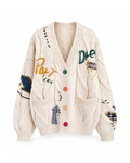 Cream embroidered cable knit cardigan, front view: four green, coral, peach and red buttons, yellow and green stitched lettering, plaid and navy patches, two patch pockets